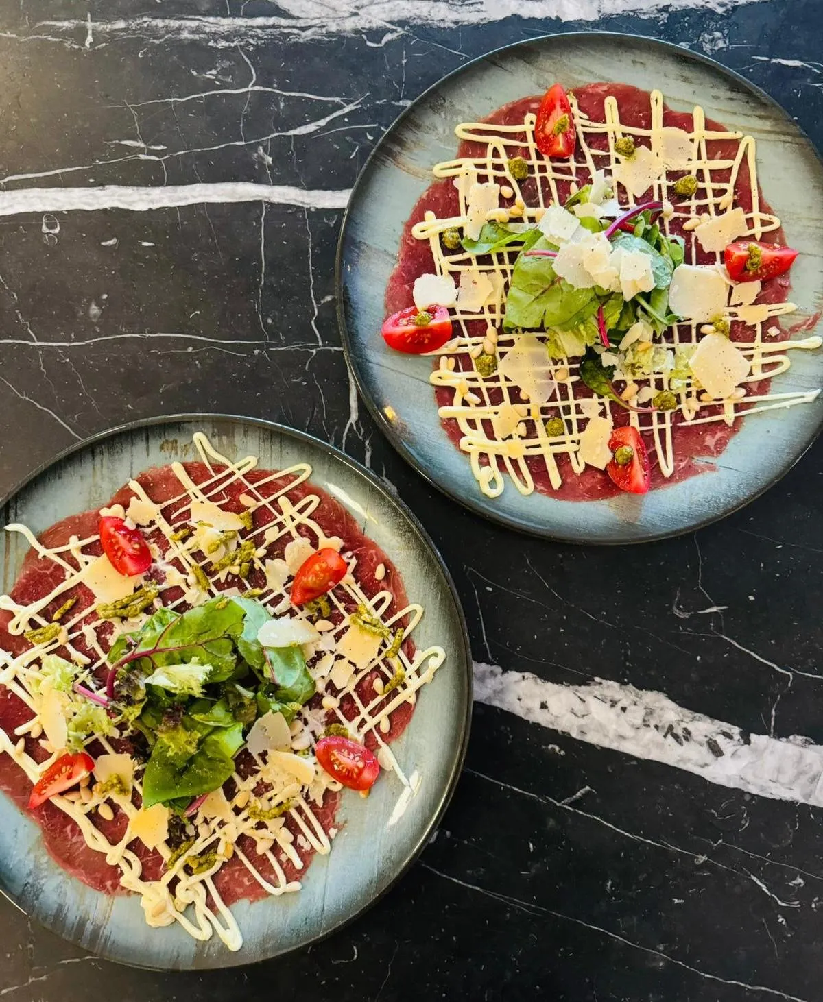 Twee borden carpaccio met Parmezaanse kaas, pijnboompitten, sla en truffelmayonaise