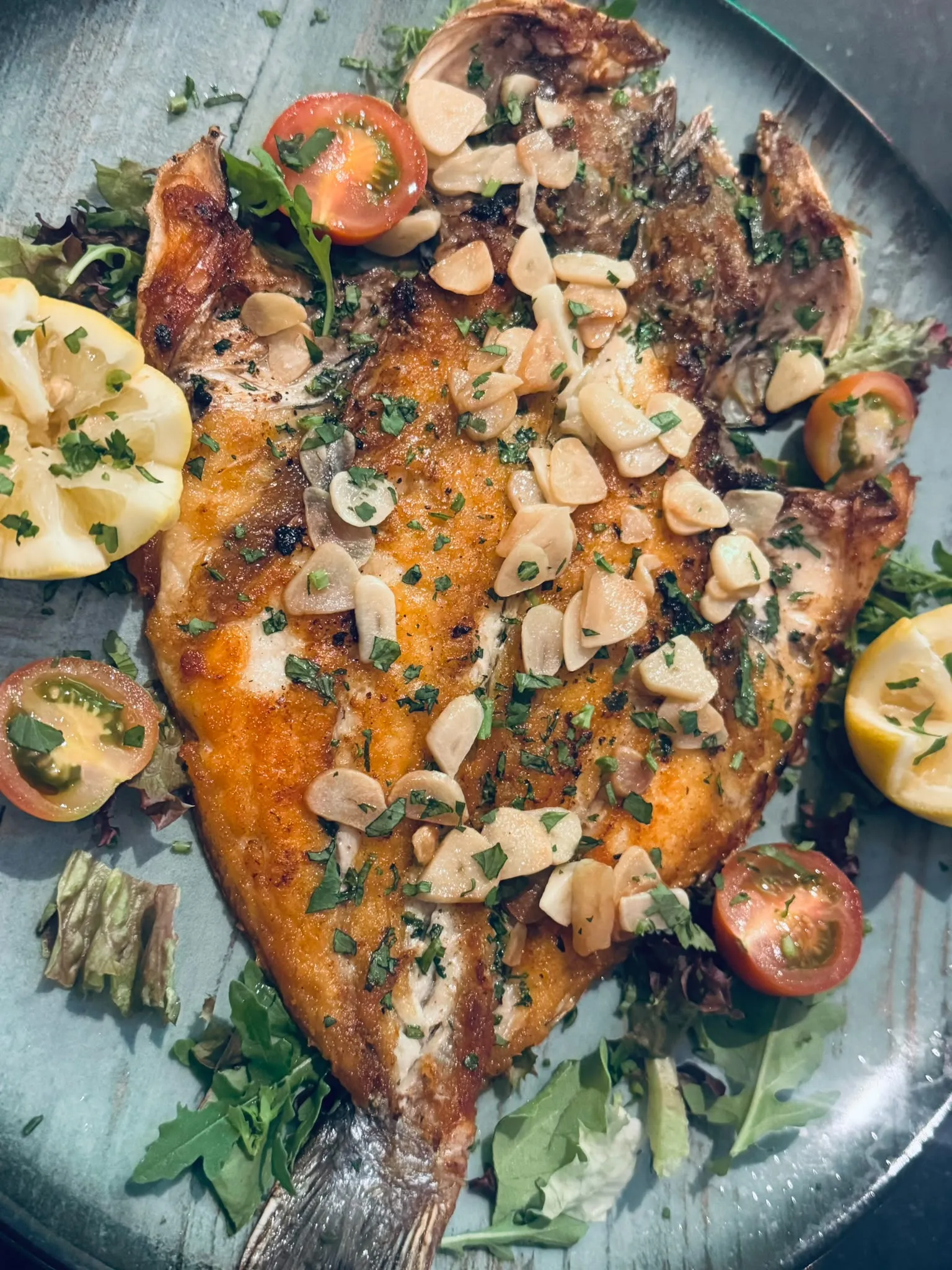 Een hele gegrilde dorada bij Darna met plakjes knoflook en verse kruiden, met salade en een partje citroen ernaast