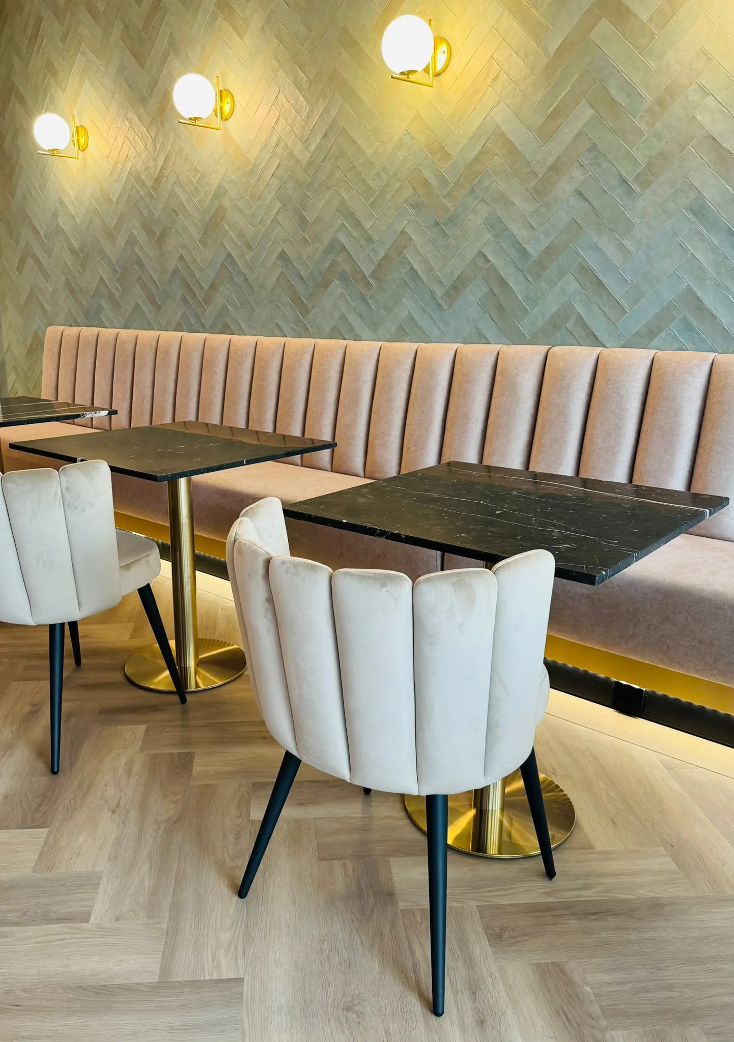 Crèmekleurige velours stoelen met gouden voet rond zwart marmeren tafels, voor een beige velours bank