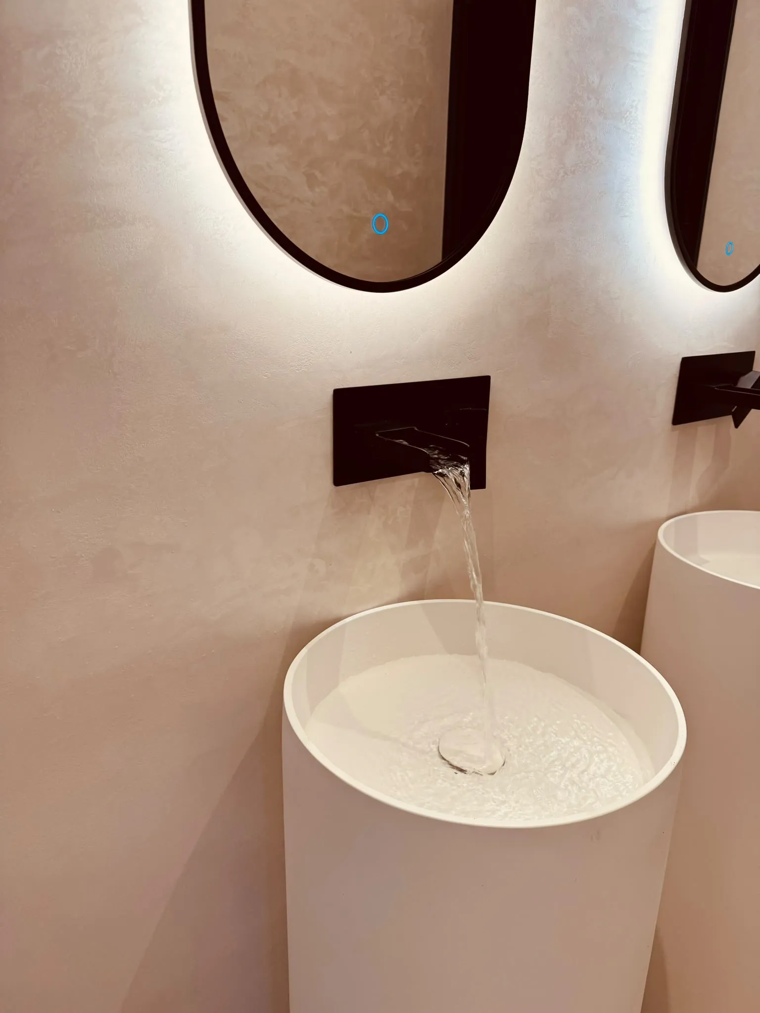 De wasruimte met een vrijstaande ronde wastafel, een zwarte wandkraan en een ovale spiegel met verlichting achter de rand