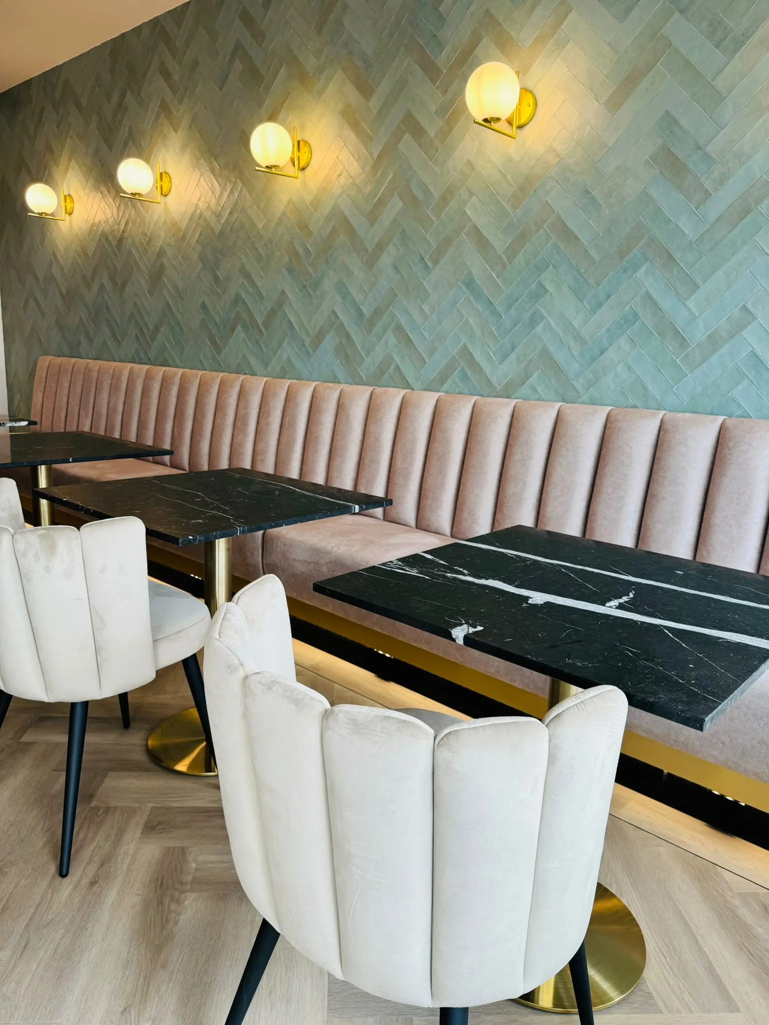 De eetzaal van Darna met een zeegroene zellige-visgraatwand, gouden wandlampen, een lange velours bank en zwart marmeren tafels