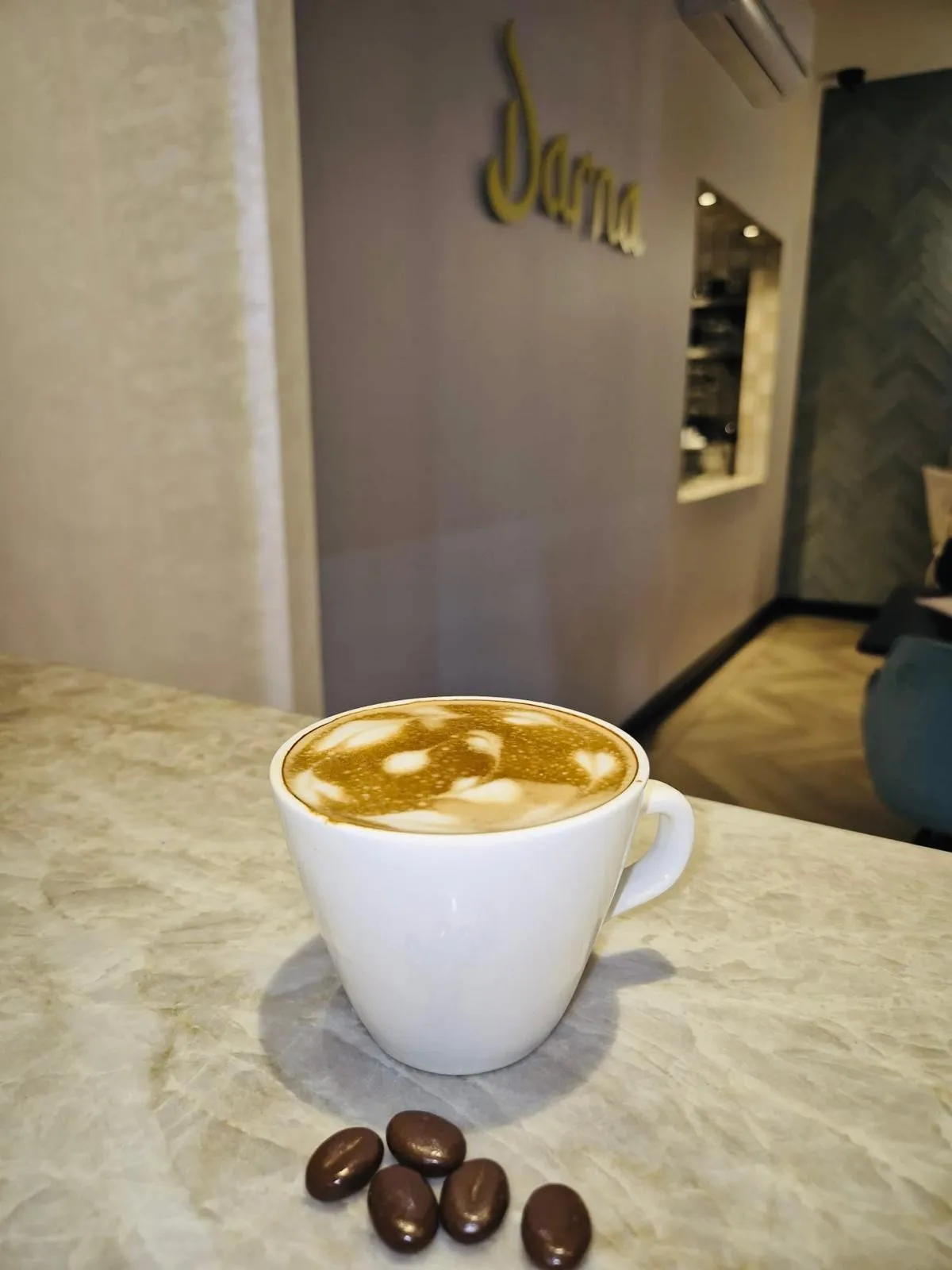 Een cappuccino met latte art in een witte kop op de bar bij Darna, met een paar koffiebonen ernaast