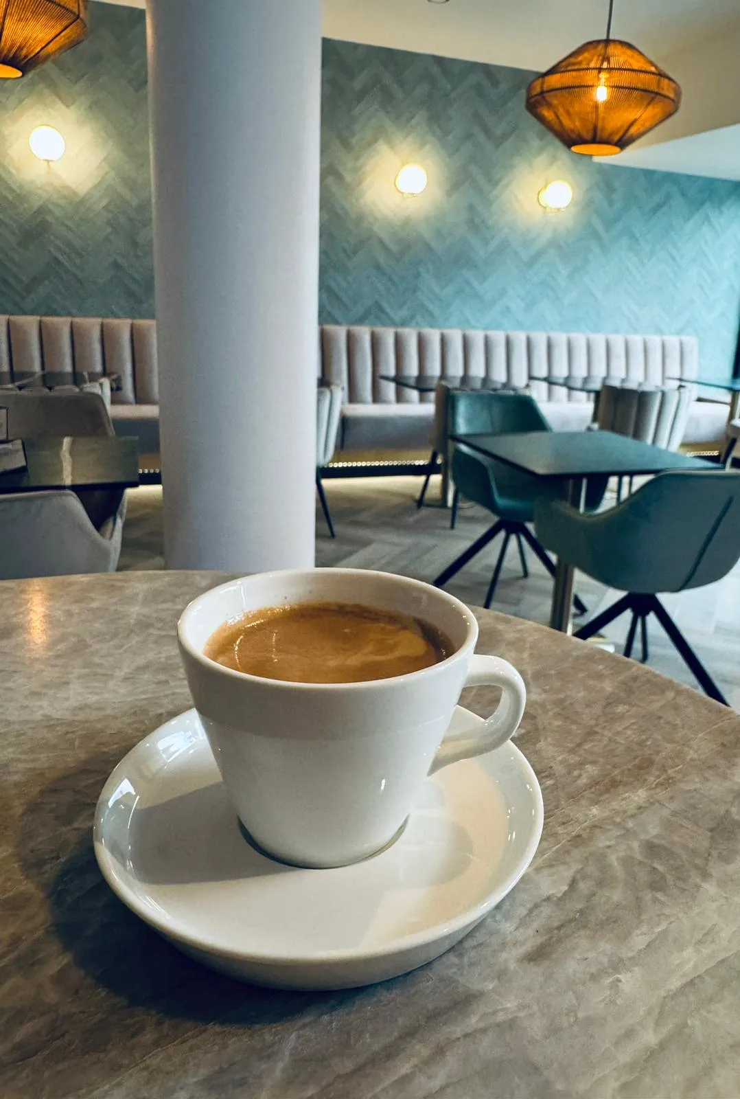 Een kop koffie op een marmeren tafel, met op de achtergrond de zeegroene zaal van Darna