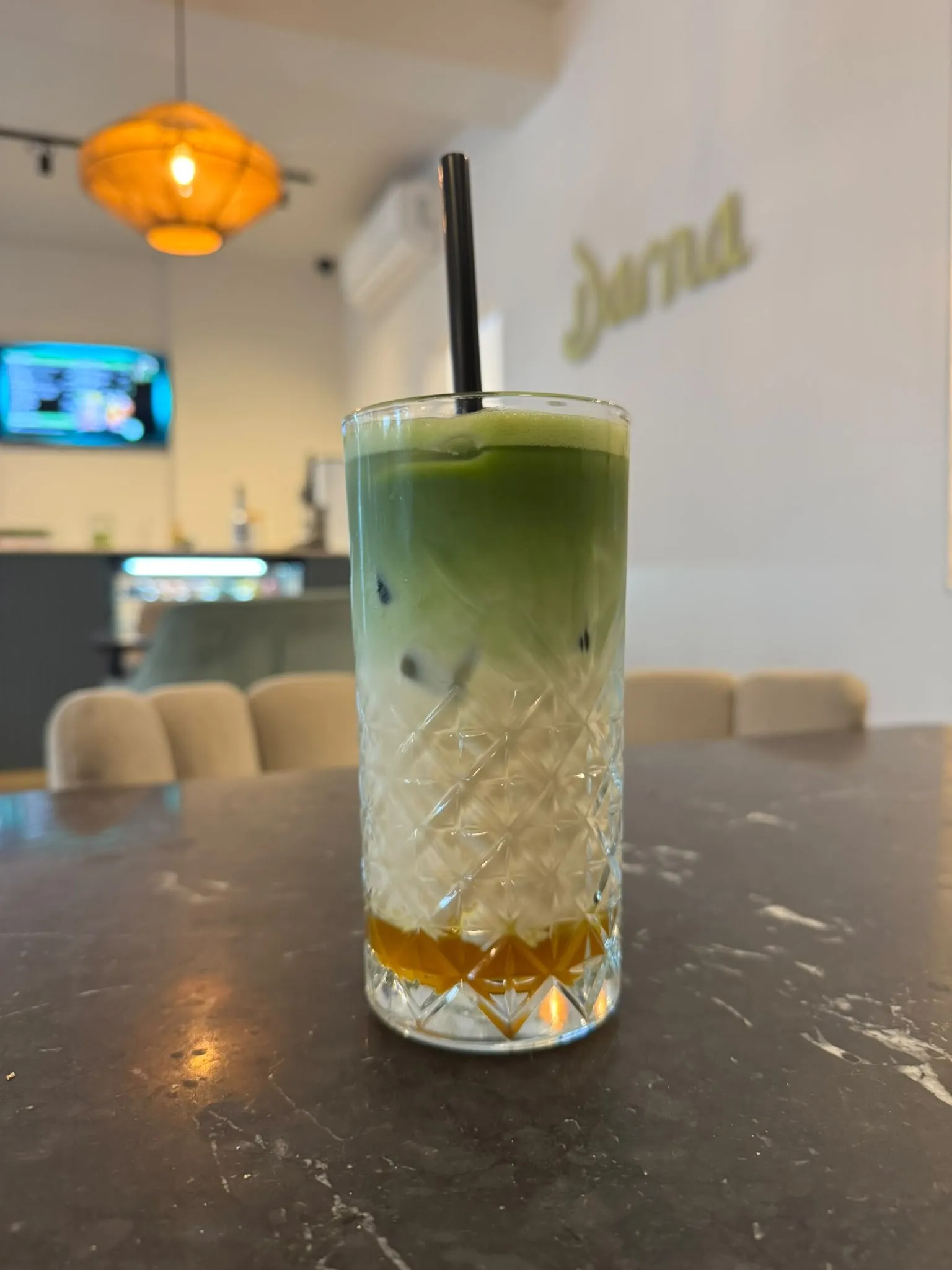 Een hoog kristallen glas groene matcha bij Darna: siroop onderin, daarboven melk en een laag felgroene matcha, met een zwart rietje
