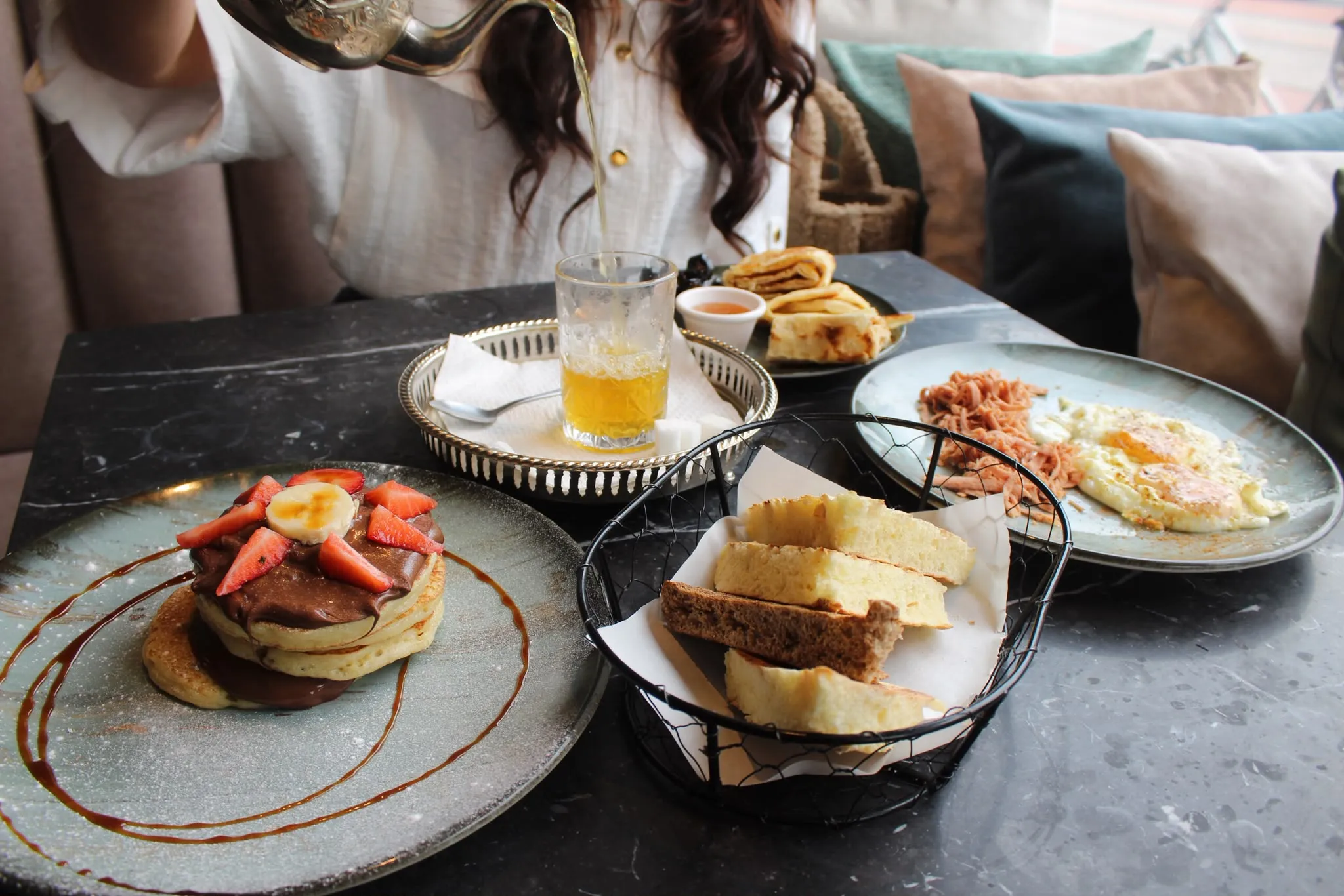 Ontbijttafel bij Darna met pancakes met aardbeien, een mandje vers brood, msemen en verse muntthee die wordt ingeschonken