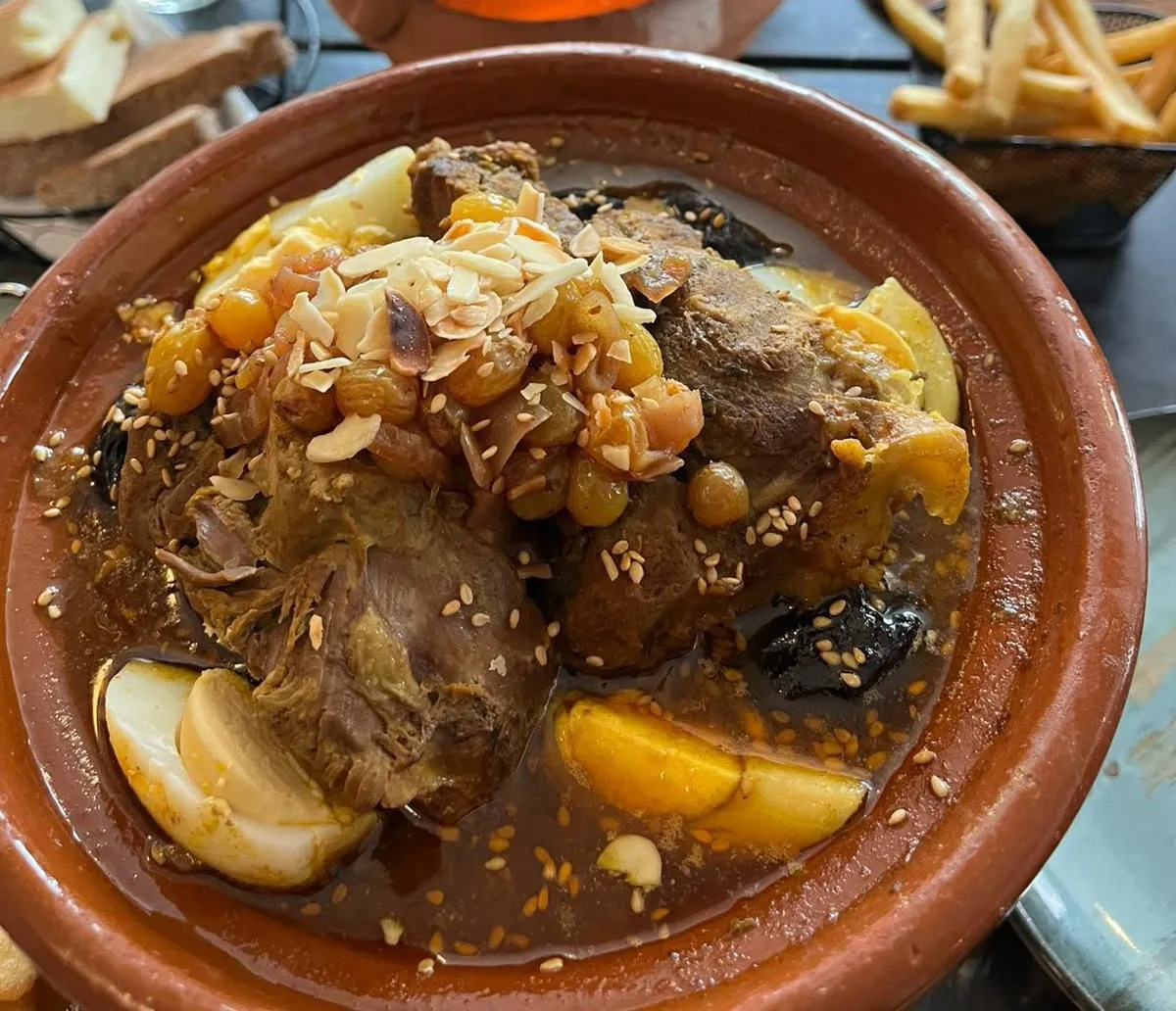 Lamstajine bij Darna in de aardewerken schaal: mals lamsvlees met pruimen, rozijnen, amandelschaafsel en sesam, met op de achtergrond een tajine kip